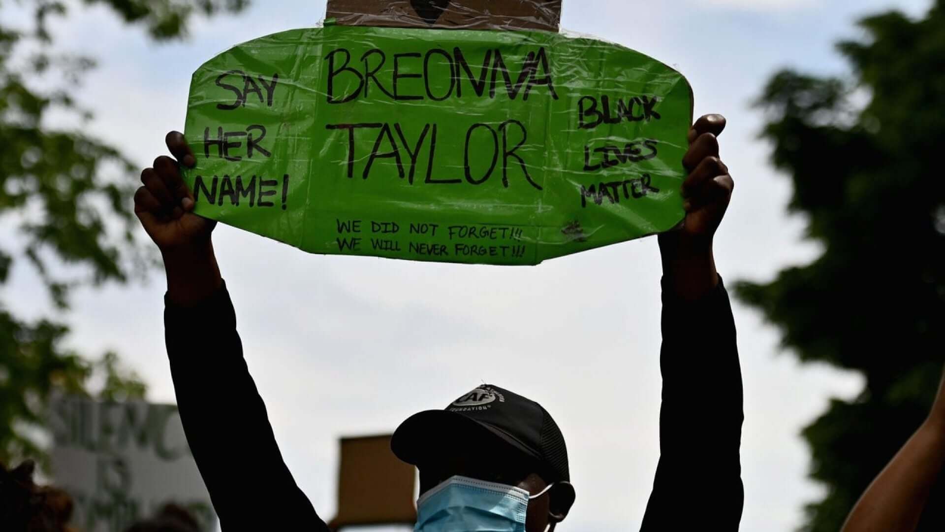 Person holding green hand made sign saying, Breonna Taylor, Say her name