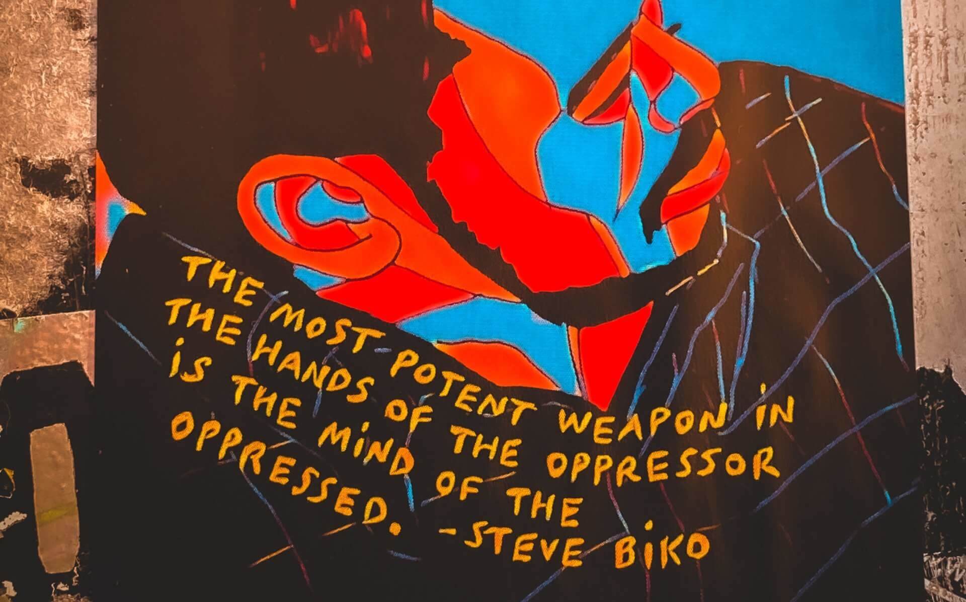 Healing Justice - Illustration with red and blue geometric shapes with showing a person with beard a quote written on the shoulder saying, the most potent weapon in the hands of the oppressor is the mind of the oppressed. - steve biko