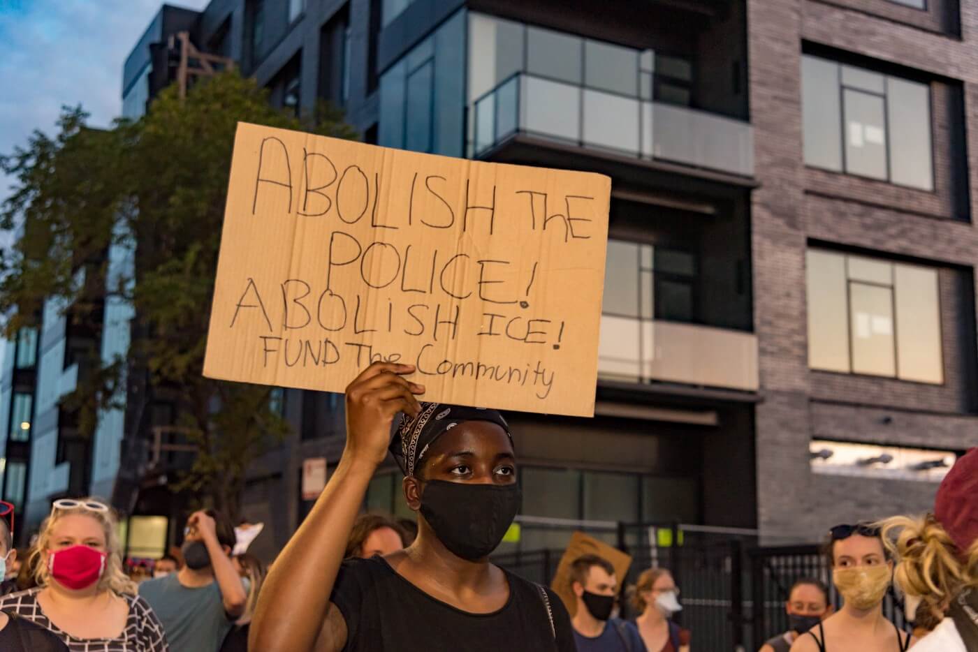 people marching and a black protestor holding cardboard sign that says Abolish the Police, Abolish ICE