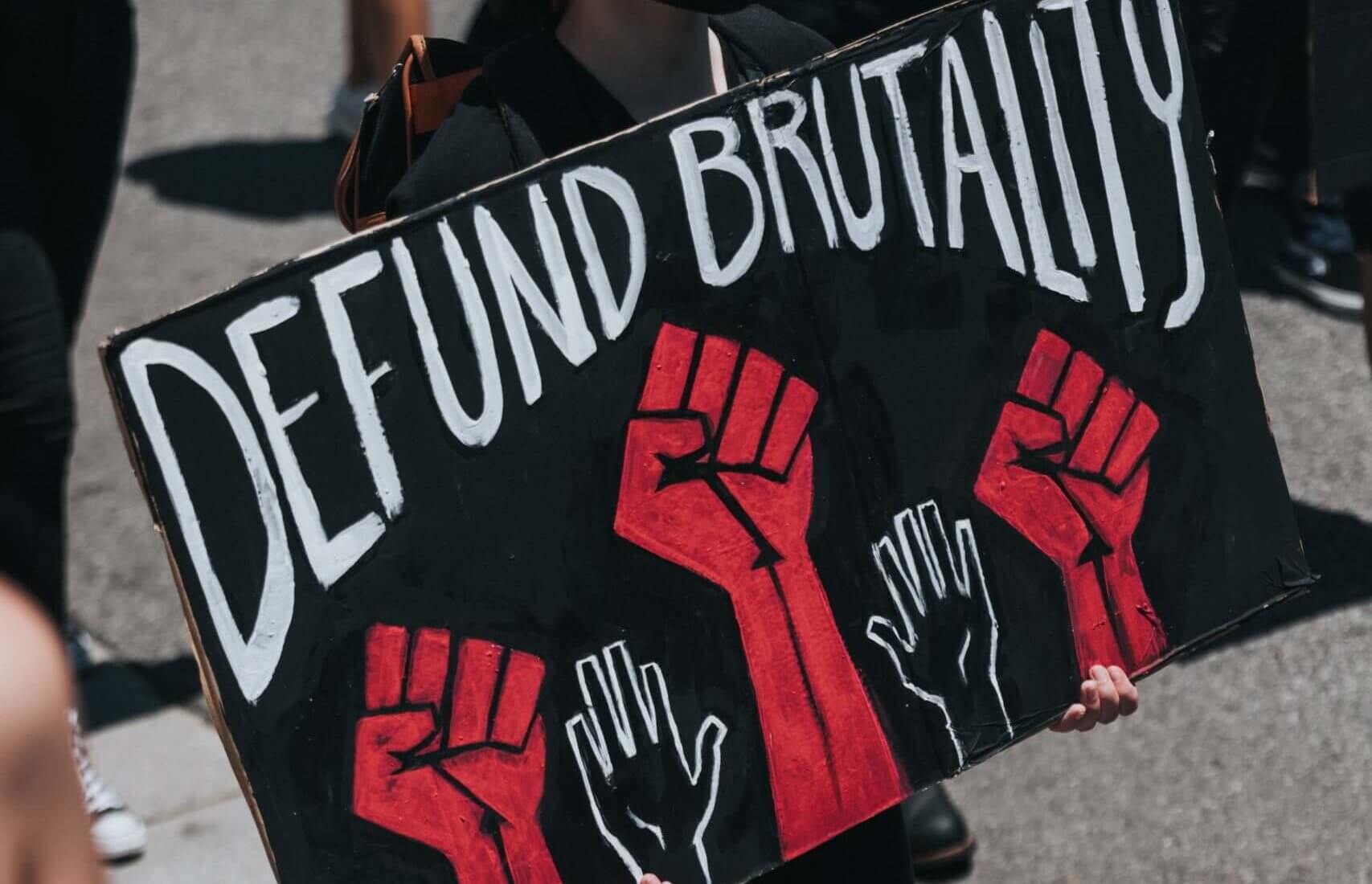 hand written sign that says, "Defund Brutality" and drawings of red fist raised