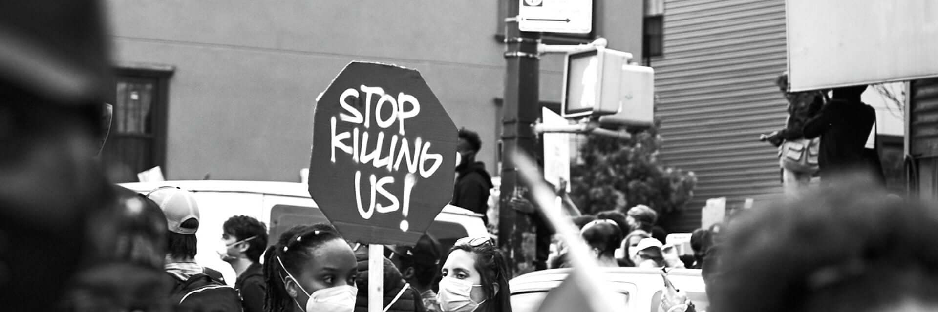 Defund the police protest with protestor holding stop sign shaped sign that says, Stop Killing Us